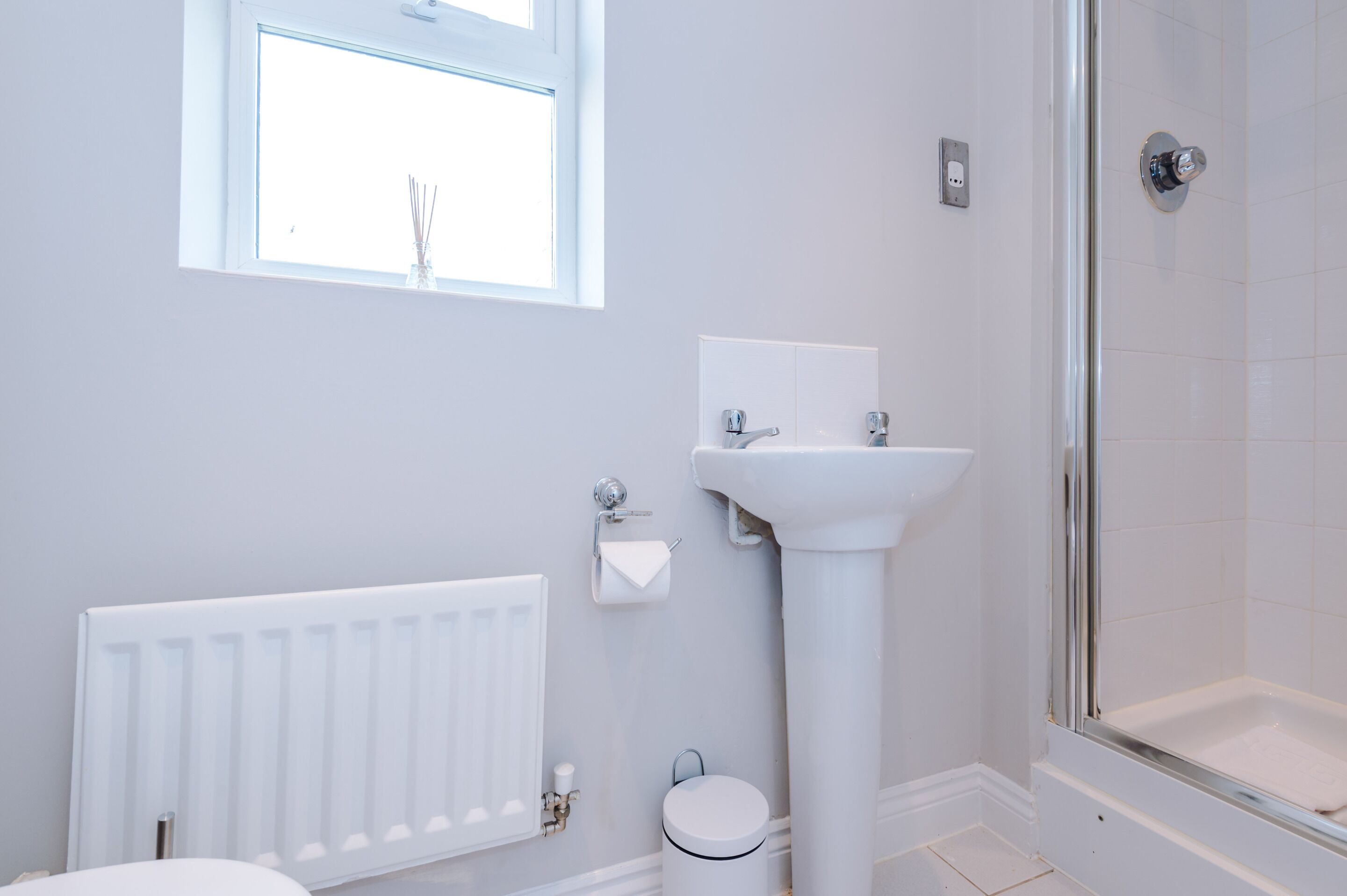 Une salle de bain avec un radiateur blanc, un lavabo, des toilettes et une douche.