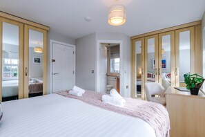 Hotelkamer met een groot bed, een bureau, een stoel en een spiegel. Een deur leidt naar een andere kamer en een raam met uitzicht.