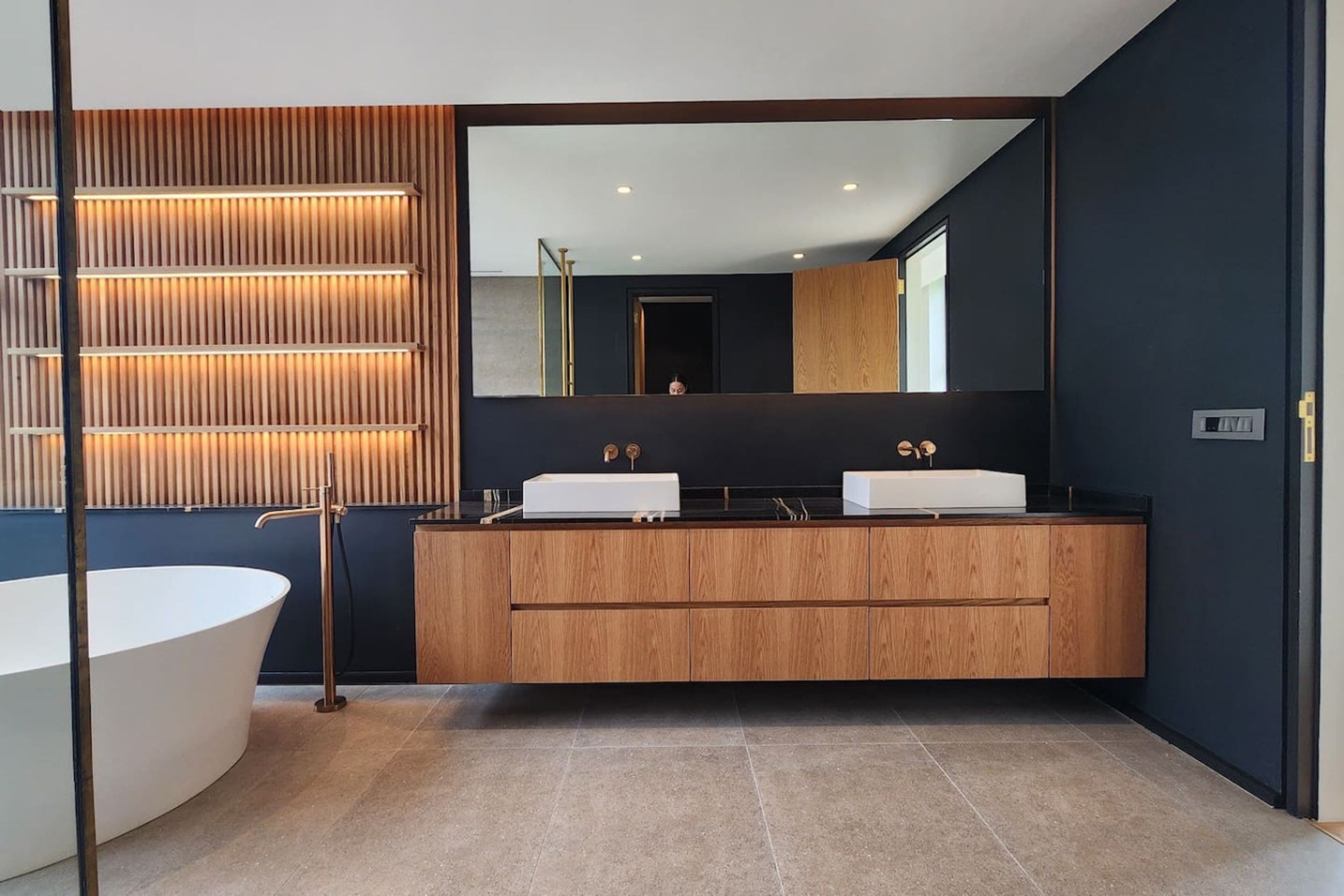 A modern bathroom with a freestanding bathtub, a wooden vanity with two sinks, and a large mirror.