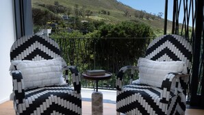 A room with two patterned armchairs, a small round table, and a view of a mountain. - Tarentaal Kloof Villa in Higgovale (Cape Town)