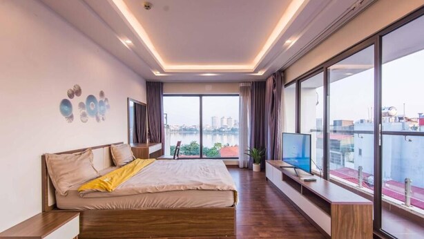 Une chambre moderne avec un grand lit, un téléviseur et une vue sur le paysage urbain, grâce à de grandes fenêtres.