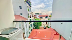 Un balcon avec un lave-linge, un bâtiment avec un toit rouge en arrière-plan et un ciel dégagé.