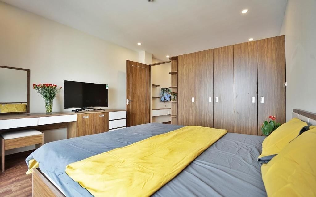 A modern bedroom with a bed, a desk, a TV, and a wardrobe.