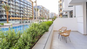 A modern residential building with a pool, outdoor seating, and lush greenery.