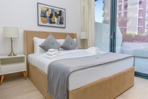 A hotel room with a bed, two bedside tables, a lamp, a painting, and a view of a building.