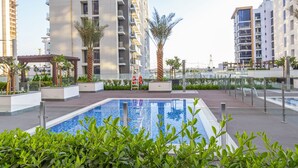 A modern residential building with a swimming pool surrounded by greenery and palm trees.