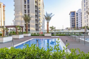 A modern residential building with a swimming pool surrounded by greenery and palm trees.