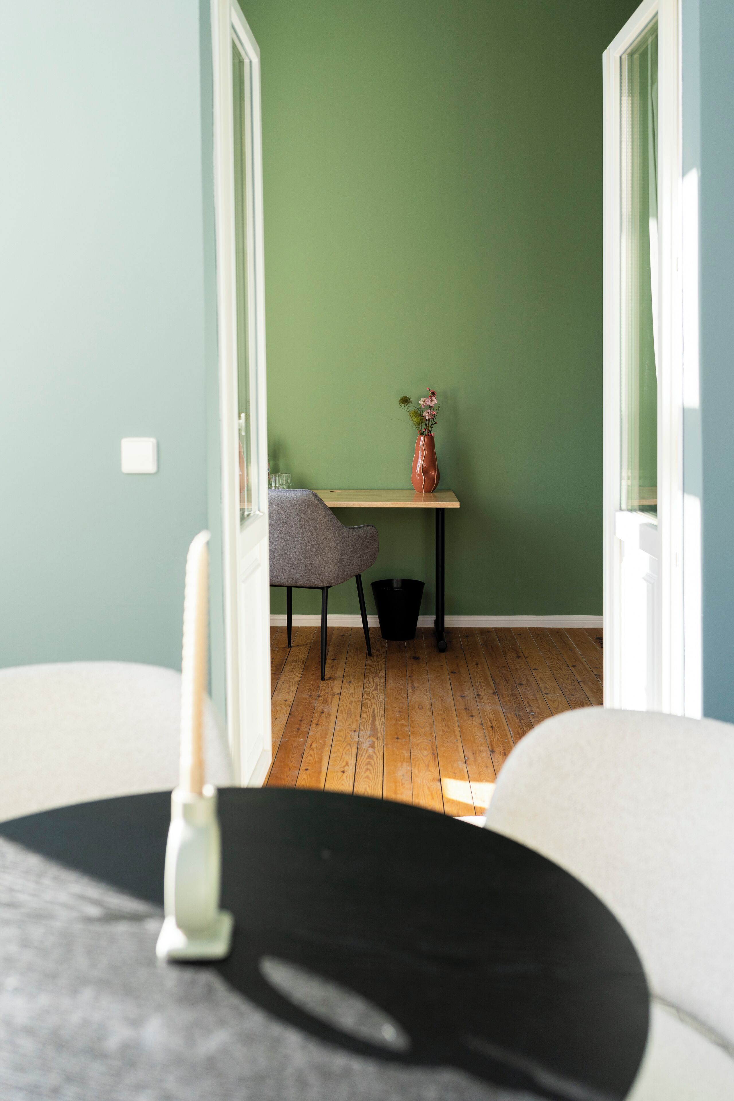 Une pièce avec un plancher en bois, une table sur laquelle se trouve un vase, et une chaise.