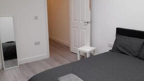 Un dormitori amb llit, una petita taula de nit, un mirall i una porta que dona a una altra habitació.