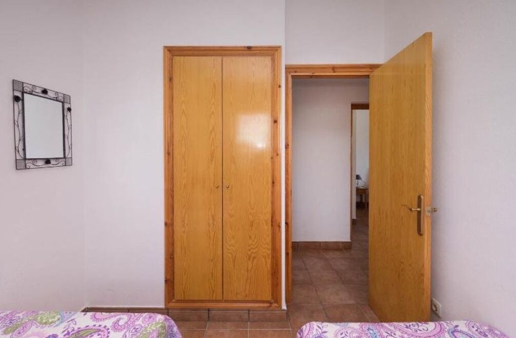 A bedroom with a wooden wardrobe, a mirror, and a bed with a patterned bedspread.