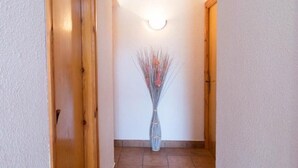En gang med en trædør til venstre, en vægmonteret lampe og en vase med tørrede blomster til højre.