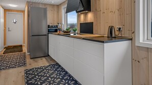 Eine moderne Küche mit Holzwandverkleidung, einem Edelstahlkühlschrank, einer schwarzen Dunstabzugshaube und einem Fenster mit Blick ins Freie.