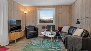 Ein gemütliches Wohnzimmer mit Fernseher, einer schwarzen Ledersofa, einem weißen Couchtisch und einem Teppich mit grünem Muster.