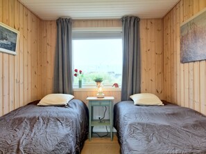 A room with two beds, a small table with a lamp, and a window with curtains.