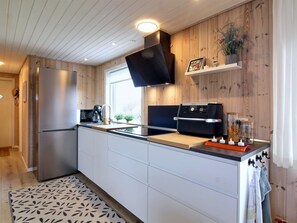 A modern kitchen with a built-in stove, a refrigerator, and wooden paneling on the walls.