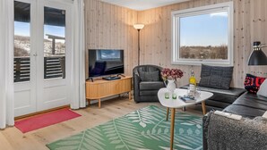 Ein modernes Wohnzimmer mit Fernseher, Sofa, Couchtisch und einem großen Fenster.