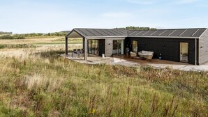 Et moderne hus med en overdækket terrasse, store vinduer og en træterrasse.