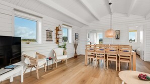 En rummelig stue med stort fjernsyn, træmøbler og et spiseområde med bord og stole.