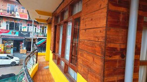 A wooden balcony with a view of a street lined with shops and a white car parked on the road. - Undiscovered Mountains Hotel (Banjar)