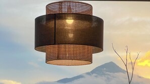 Et udendørs siddeområde med hængende lampe, stole og parasoller, med udsigt til et bjerglandskab.