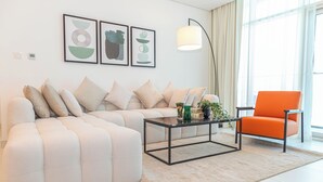 A modern living room with a sectional sofa, a coffee table, and an orange armchair. There are abstract wall art pieces and a floor lamp. - Bloomfields Modern 1BR in Thalassa  (Abu Dhabi)