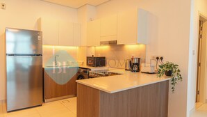 A modern kitchen with a stainless steel refrigerator, wooden cabinets, a central island, and a built-in microwave. - Bloomfields Modern 1BR in Thalassa  (Abu Dhabi)