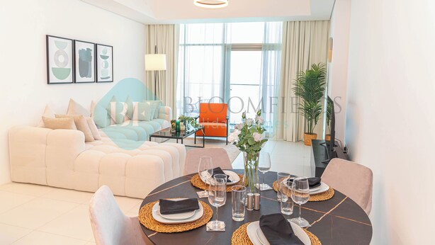 A modern living room with a sofa, a dining table set for four, and a large window with curtains. - Bloomfields Modern 1BR in Thalassa  (Abu Dhabi)