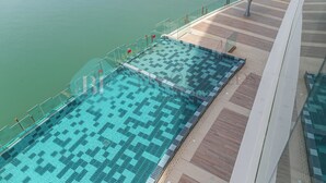 A large, rectangular swimming pool with a geometric tile pattern, adjacent to a glass railing overlooking a body of water. - Bloomfields Modern 1BR in Thalassa  (Abu Dhabi)