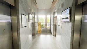 A hallway with marble walls, a yellow caution sign, and a digital display on the wall. - Apartement Urbano by NamRoom (Bekasi)