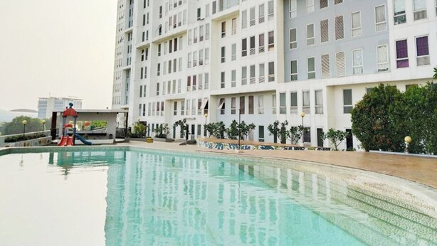 A swimming pool with a slide, surrounded by a multi-story building with balconies. - Apartement Urbano by NamRoom (Bekasi)