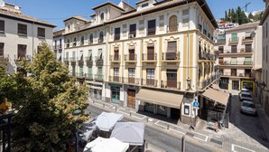 A multi-story building with balconies, a street in front, and parked cars.