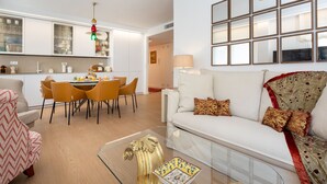 A modern living room with a glass coffee table, a sofa with patterned cushions, and a dining area with chairs and a table.