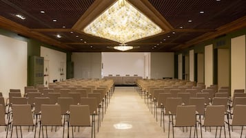 Ein Konferenzraum mit Reihen von Stühlen, einem großen Kronleuchter und einer Projektionsleinwand.
