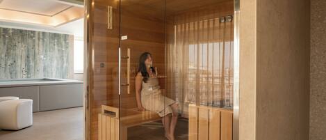 Un moderno spa con sauna de vidrio, banca de madera y sillón de masaje blanco.