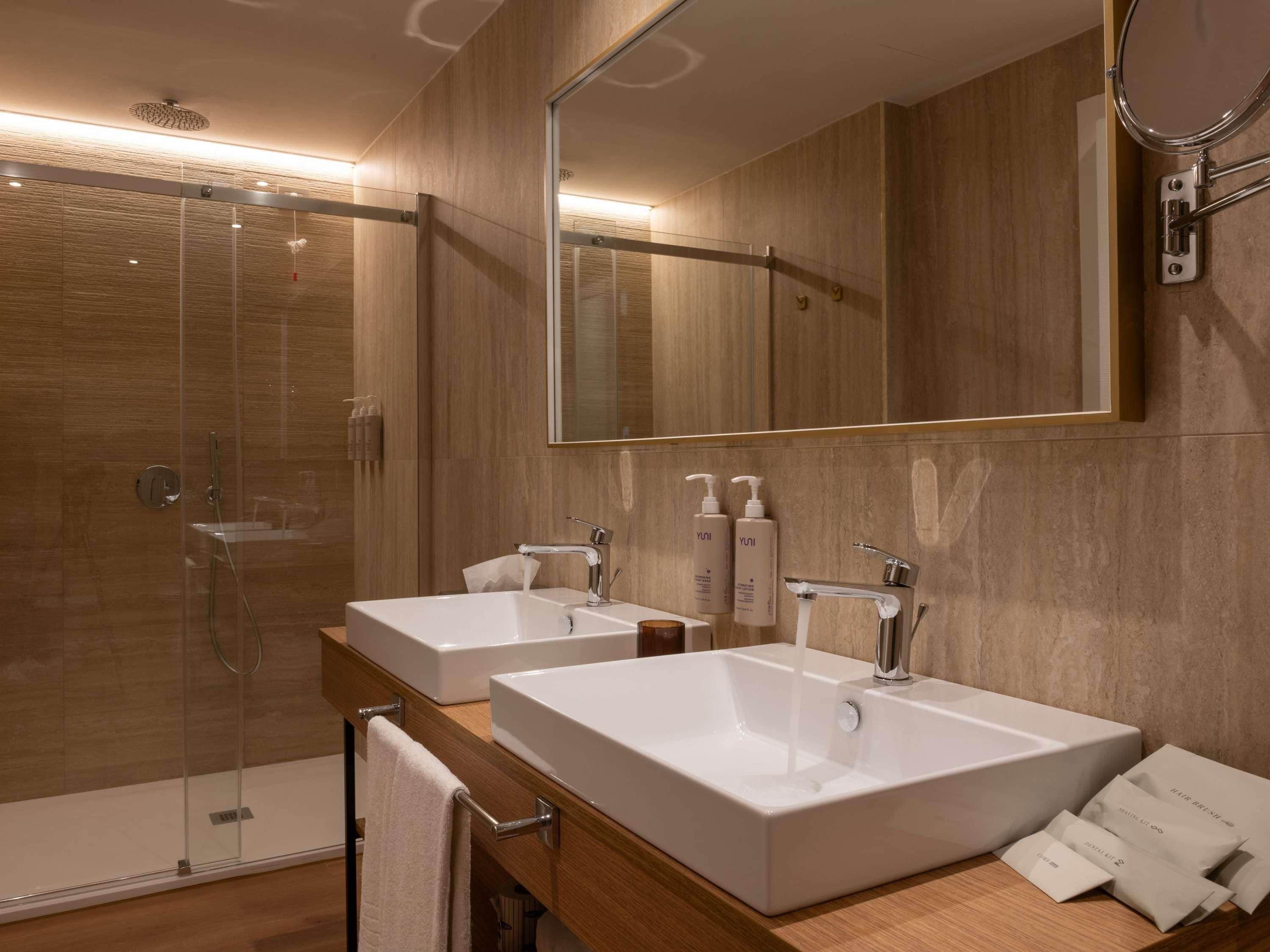 A modern bathroom with two sinks, a glass shower enclosure, and a large mirror.