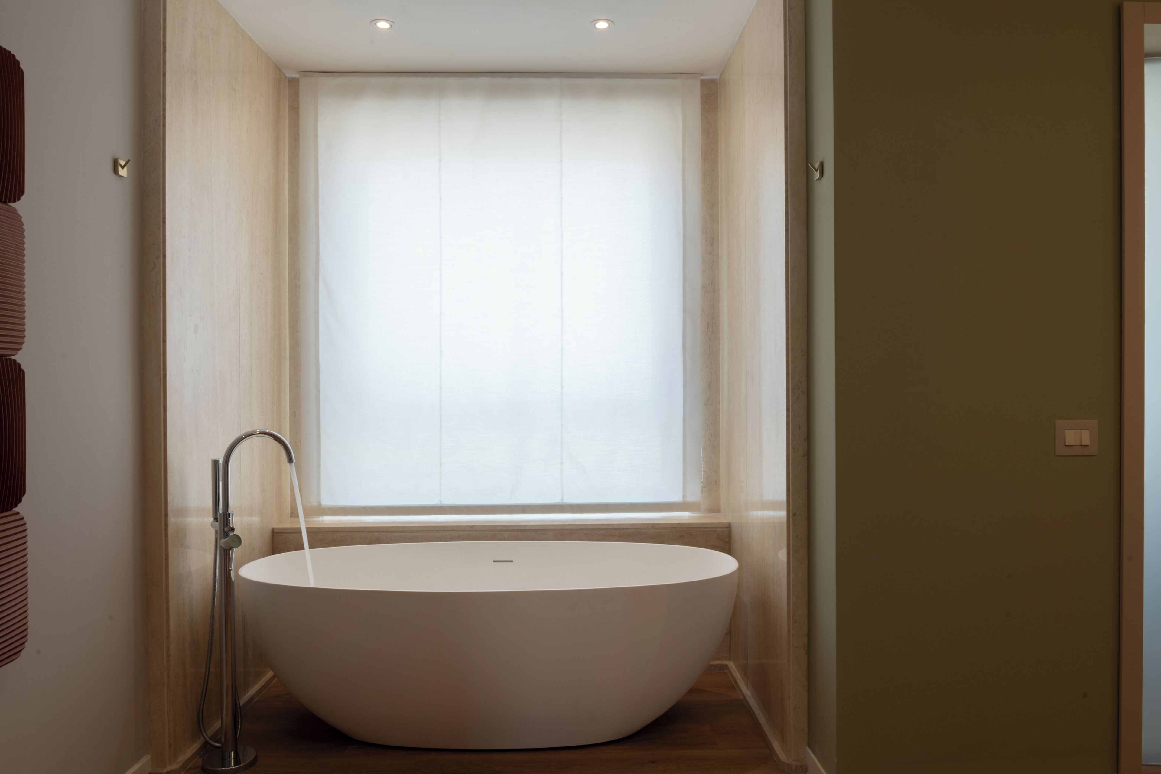 Un baño moderno con una bañera independiente, una ventana con cortinas translúcidas y suelo de madera.