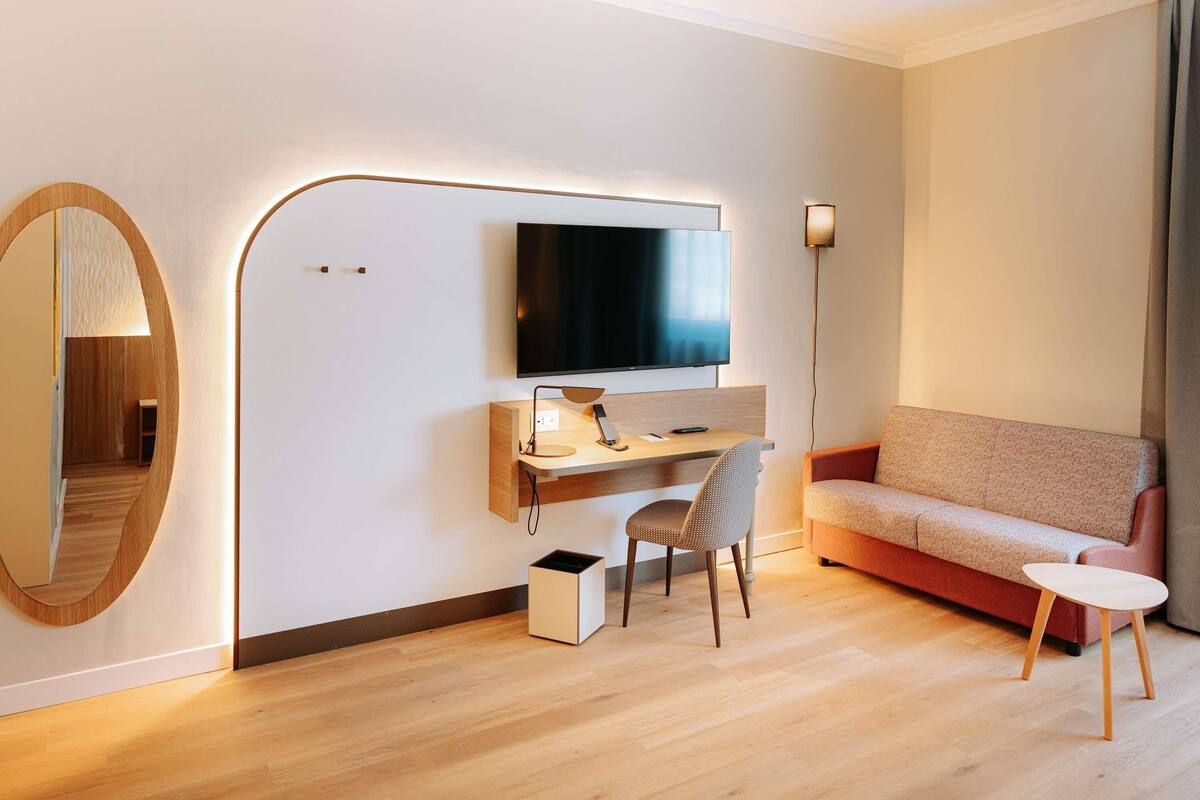 Ein modernes Hotelzimmer mit einem Holztisch, einem Fernseher, einer Couch und einem kleinen Tisch.