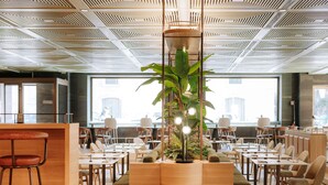 Uma sala de jantar moderna com mesas e cadeiras de madeira, um vaso central com plantas e um teto com padrão geométrico.