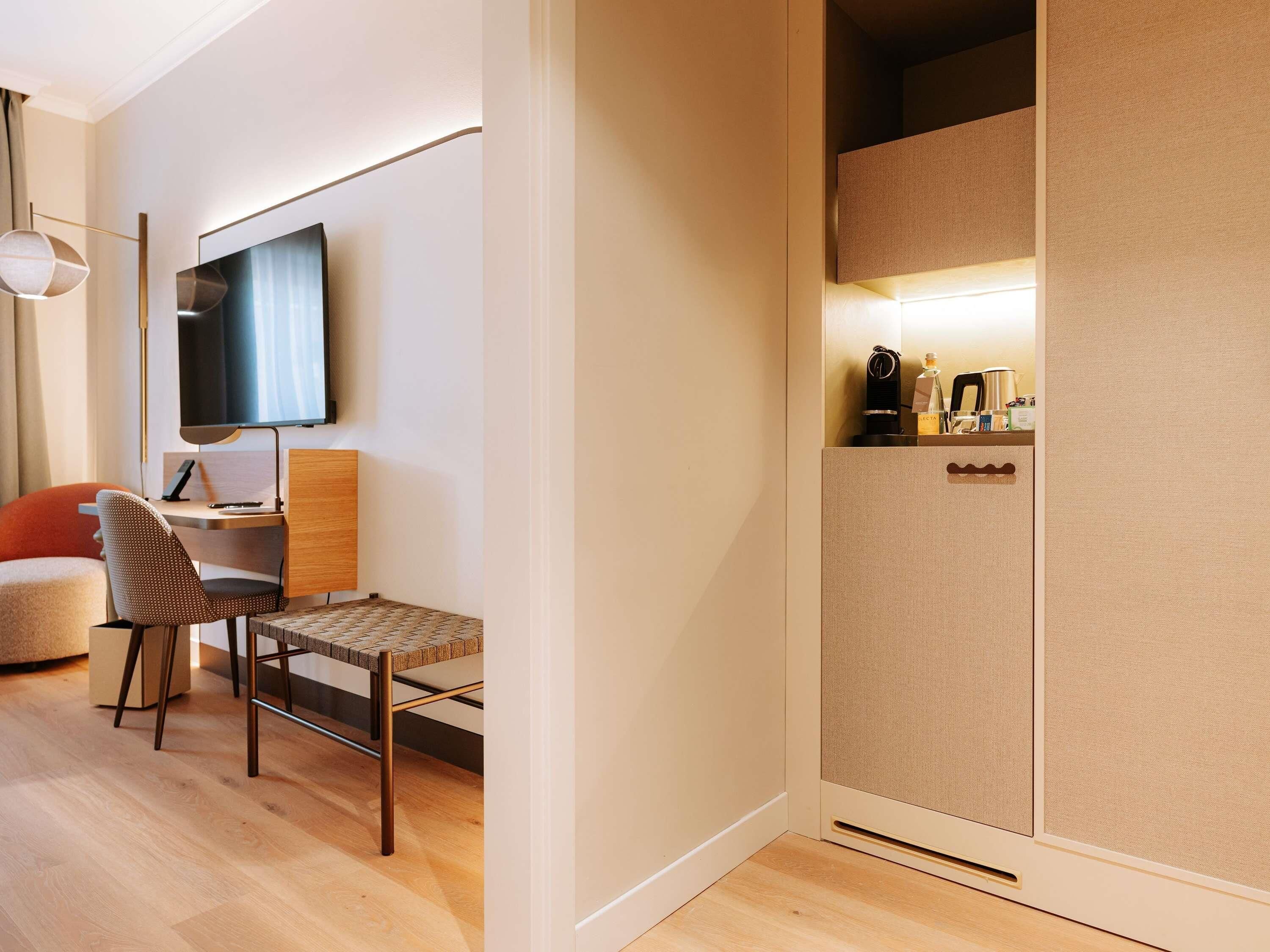 Een moderne hotelkamer met een houten bureau, een stoel, een flatscreen-tv en een minibar.