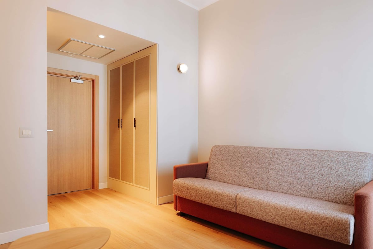 Ein Zimmer mit Holzboden, einer Couch, einem kleinen Tisch und einem Kleiderschrank mit Spiegel.