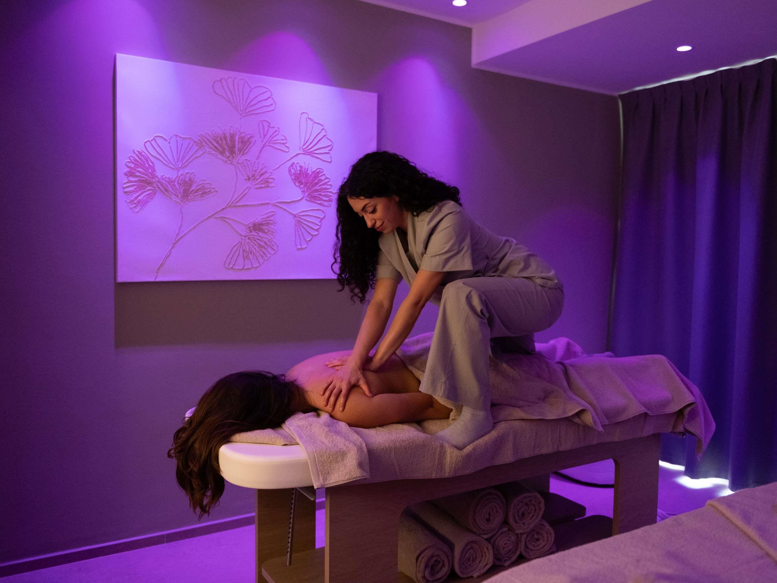A massage therapy room with a massage table, towels, and a wall-mounted floral decoration.