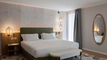 Habitación de hotel con cama, mesita de noche, lámparas fijadas a la pared, un espejo y un tapete estampado.