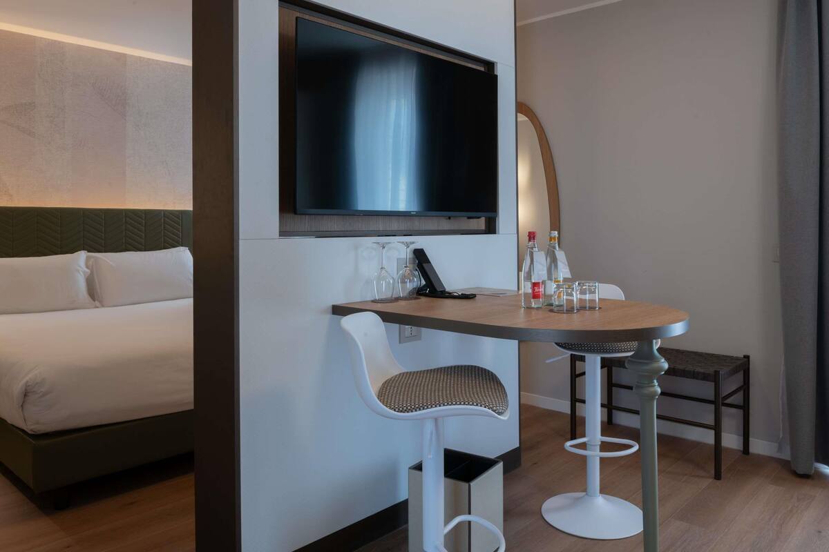 Ett modernt hotellrum med en säng, en tv som är monterad på väggen, ett litet runt bord med två stolar och en minibar.