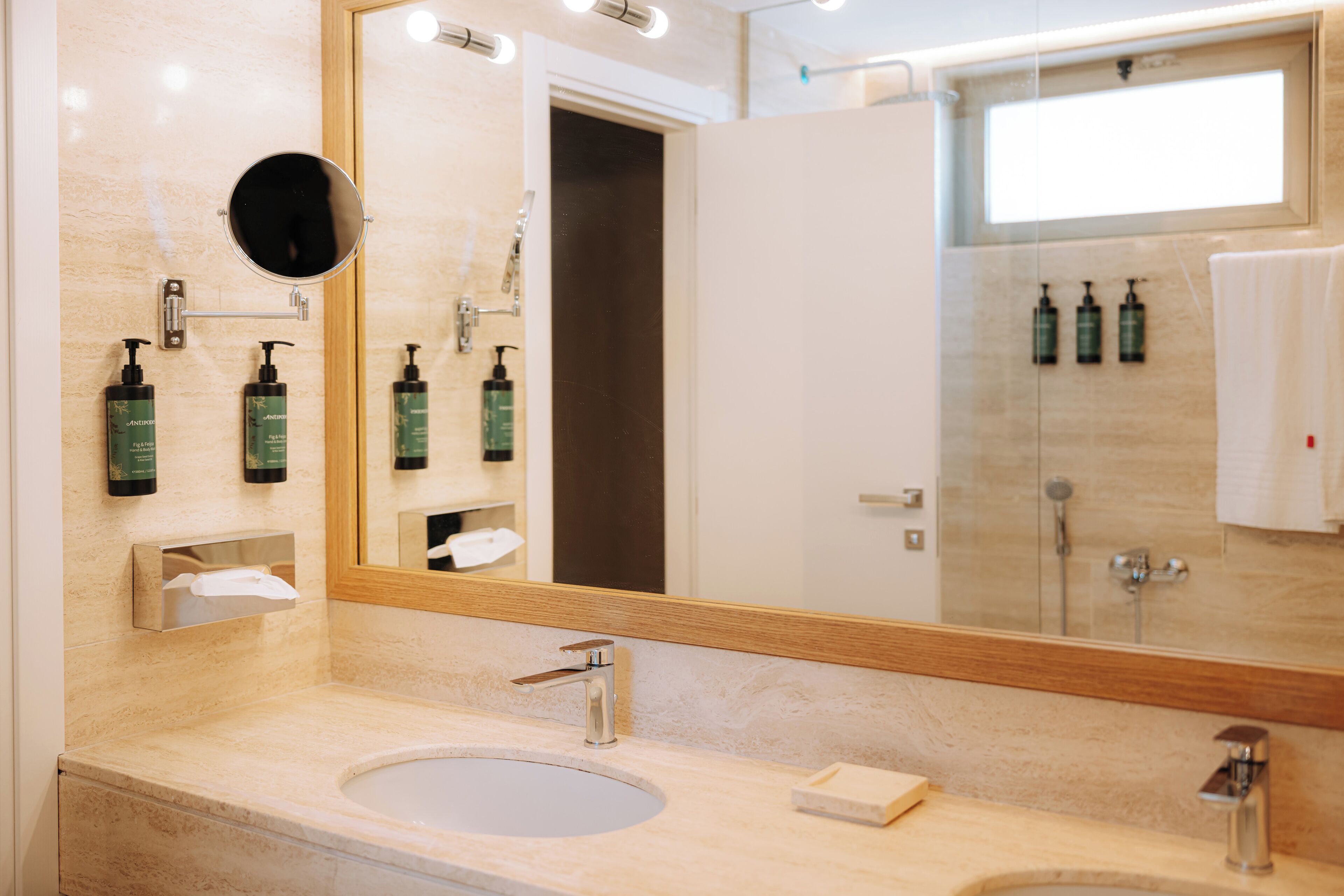 A modern bathroom with a large mirror, two sinks, and toiletries on the wall.