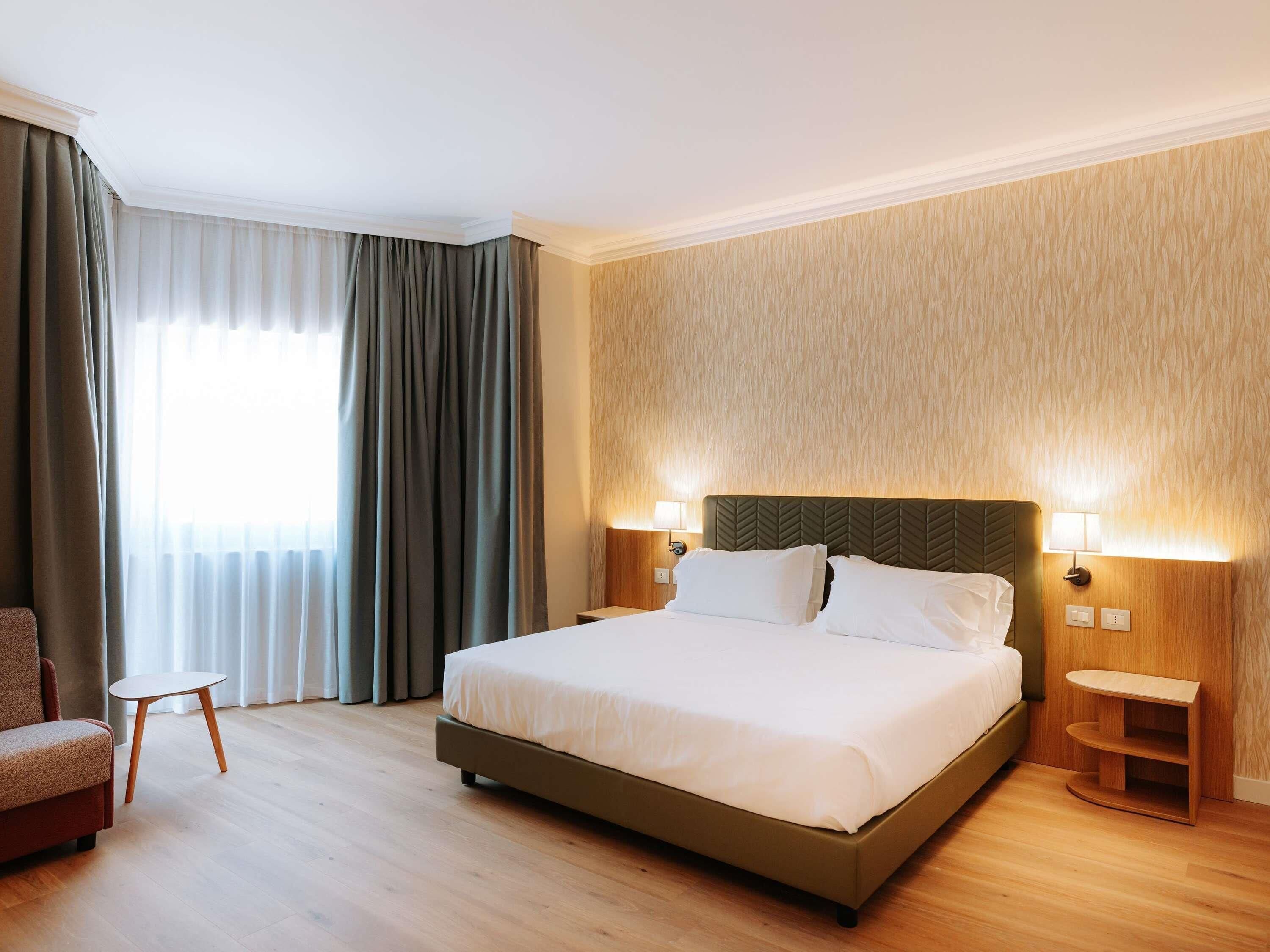 Una camera d'albergo con un letto, una sedia, un comodino e una lampada.