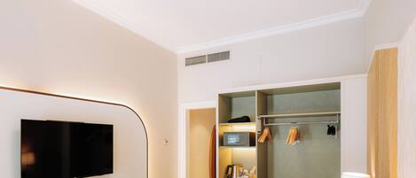 A hotel room with a bed, a TV mounted on the wall, a minibar, and a walk-in closet.