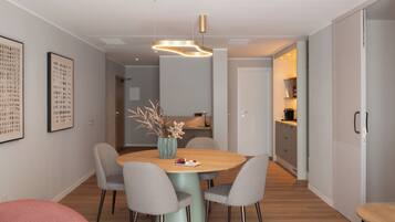 Un espace repas moderne avec une table ronde, quatre chaises, un vase de fleurs et un luminaire suspendu.
