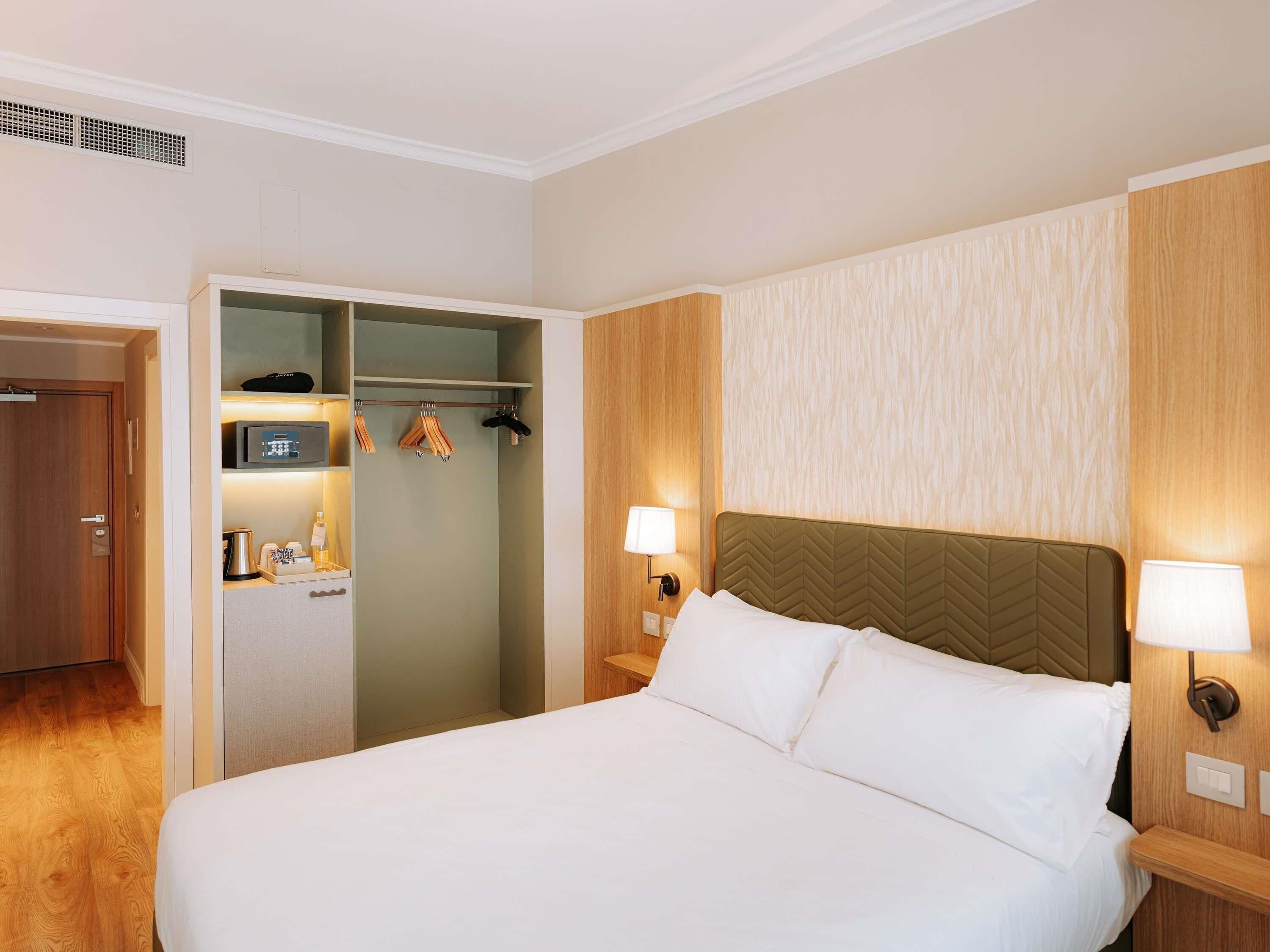 Una camera d'albergo con un letto, due lampade ai comodini, un armadio e un angolo cottura.