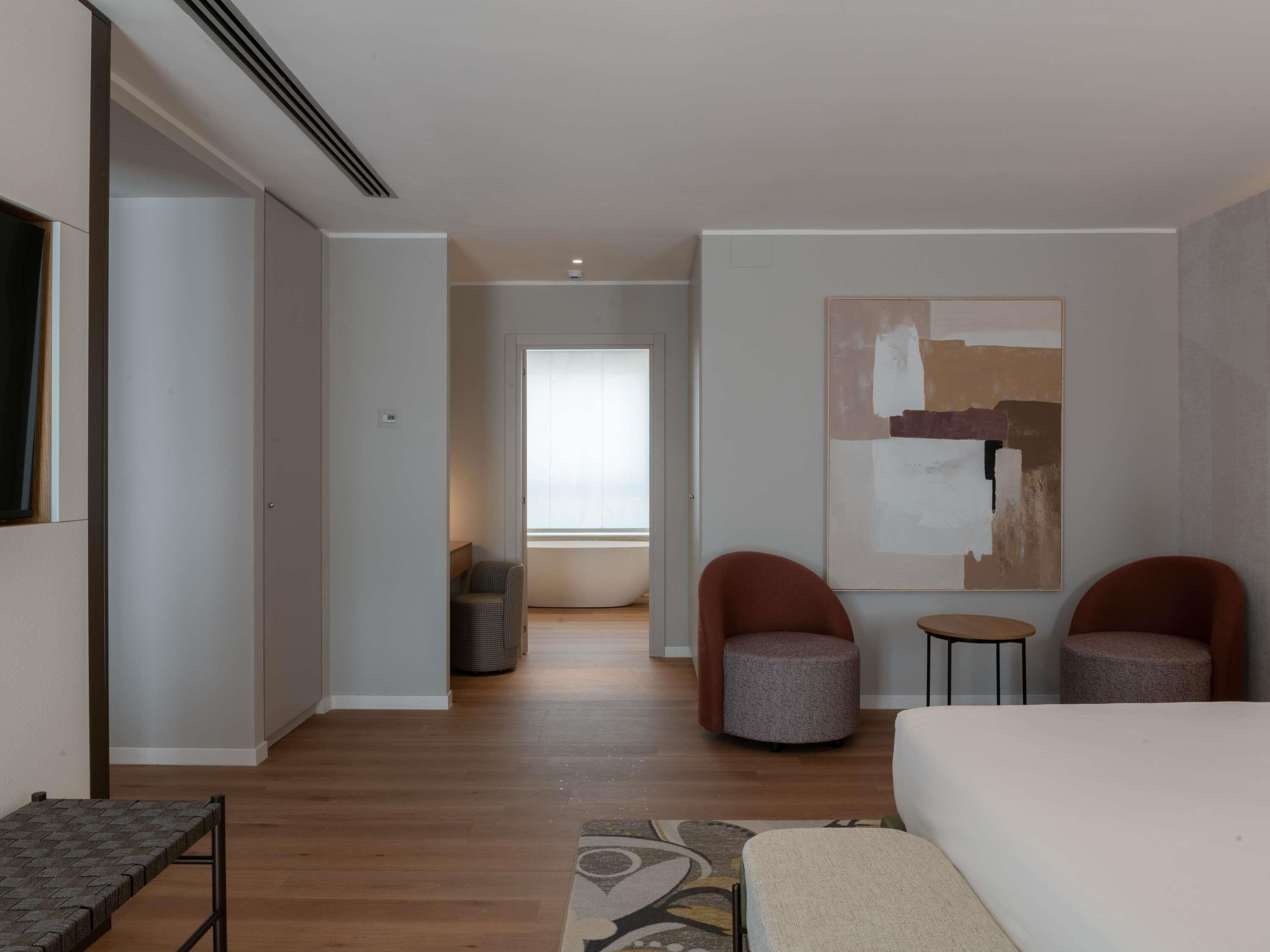 Habitación de hotel moderna con una cama grande, dos sillones, una mesita y un cuadro abstracto de gran formato en la pared.