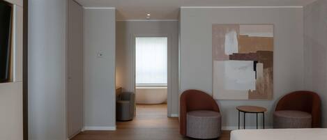A modern hotel room with a large bed, two armchairs, a small table, and a large abstract painting on the wall.